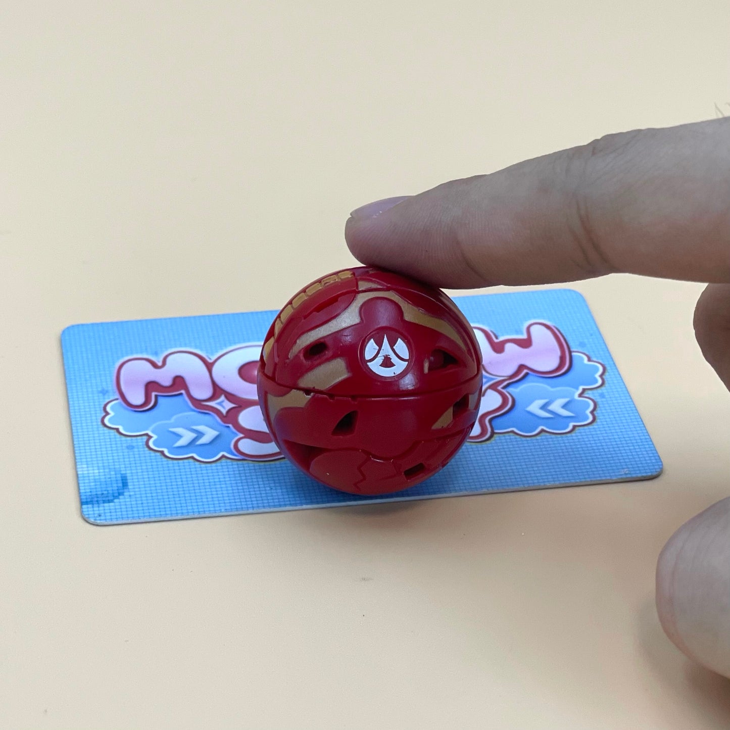 A hand is holding a red toy, which appears to be a small, round object, on a blue and pink card with a cartoon-like design.