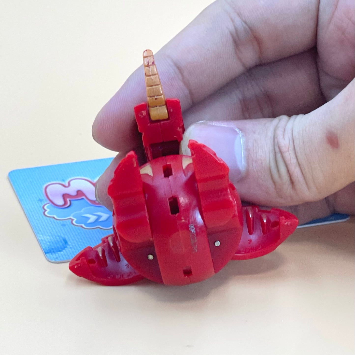 A hand is holding a red toy with a yellow horn, which appears to be a toy car or toy vehicle.