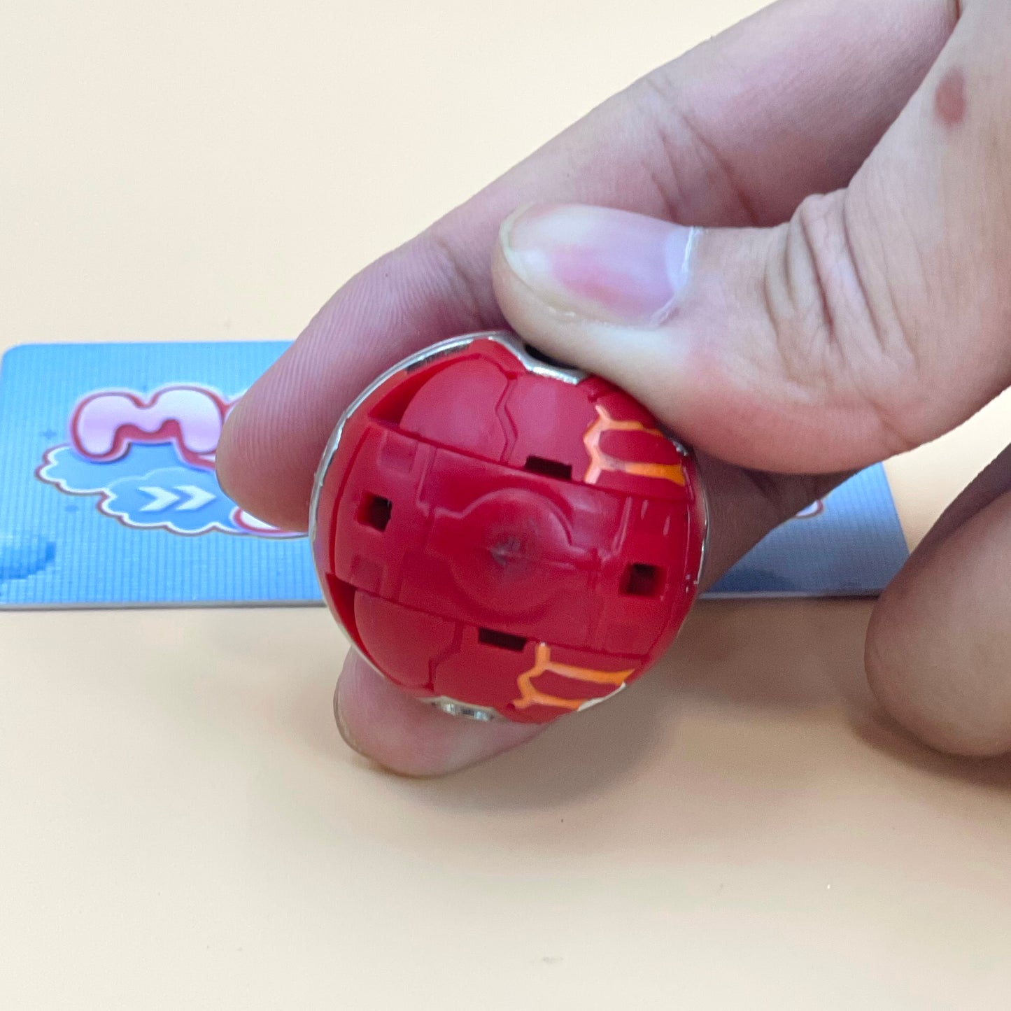 A hand is holding a red and yellow toy in the shape of a ball, with the toy's lid partially open.