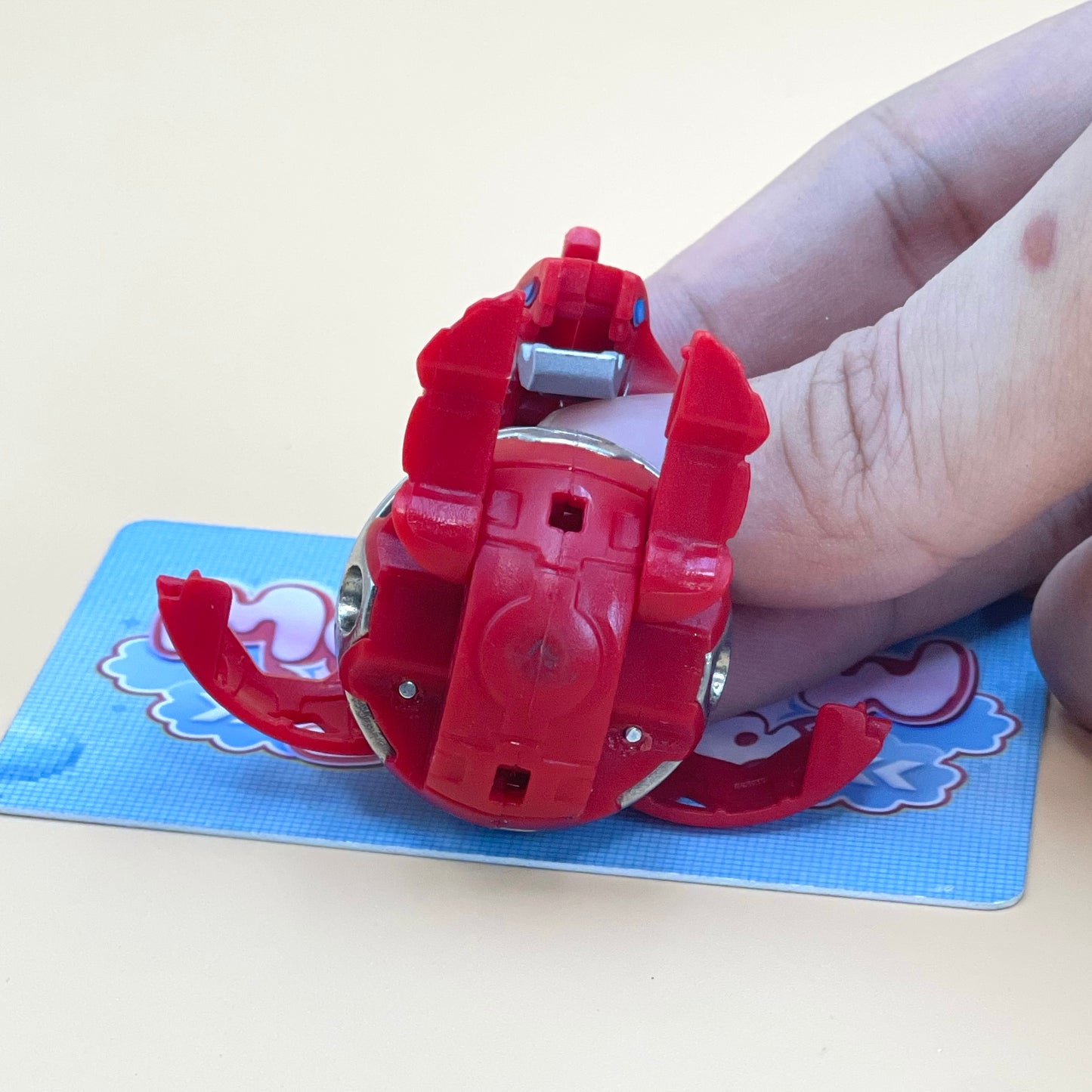 A person's hand is holding a red toy with its arms and legs spread out, positioned on a blue surface.