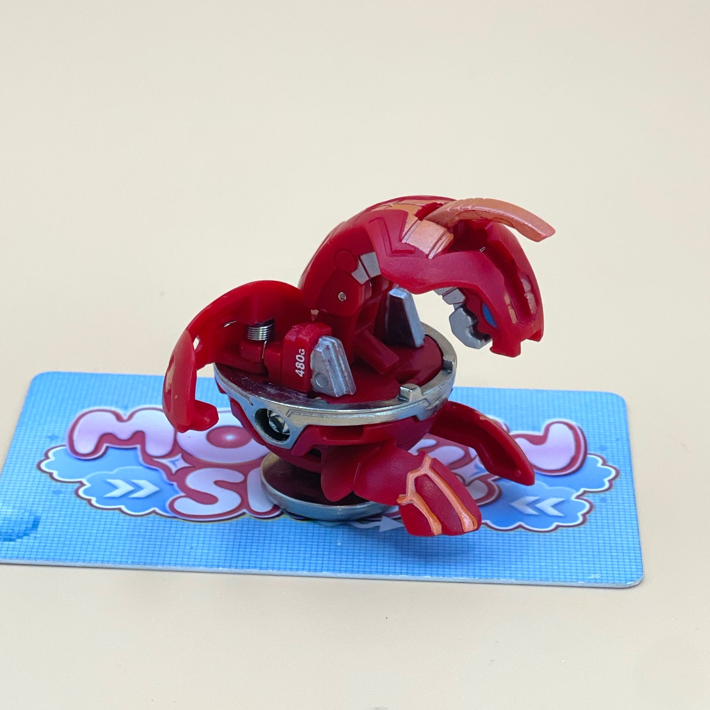 A red toy with a metallic appearance is sitting on a blue and pink checkered surface.