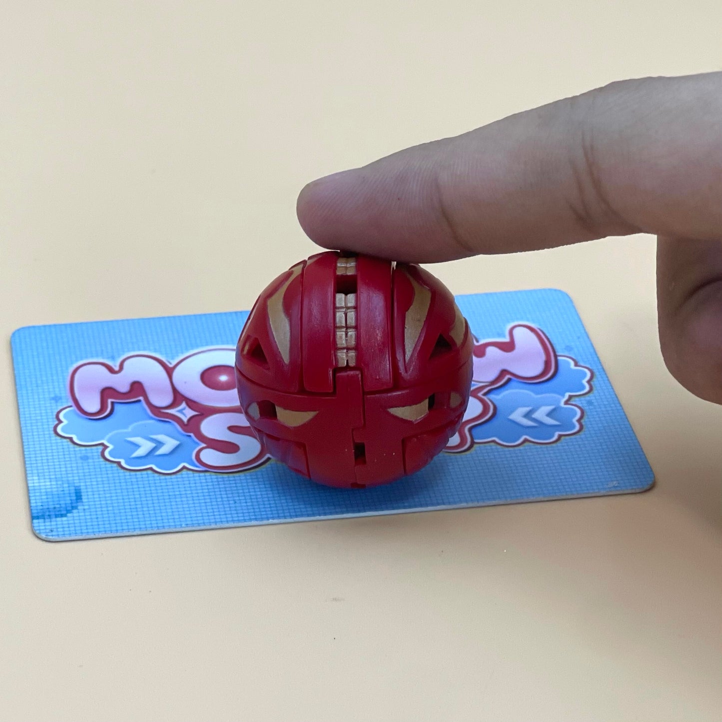 A hand is holding a red toy in the shape of a ball, which is placed on a blue card with a cartoon character design.