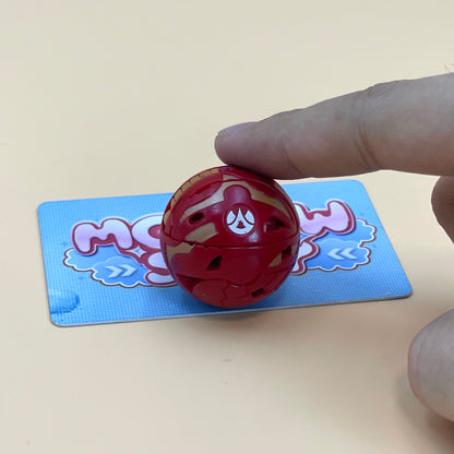A hand is holding a red toy, which appears to be a small, round object, on a blue and pink card with a cartoon-like design.