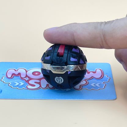 A hand is holding a small, black and purple toy ball with a red button on it, placed on a blue and white patterned surface.