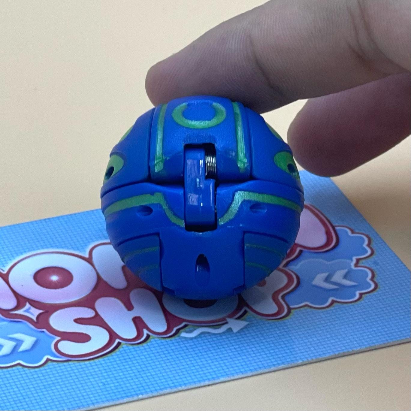 A hand is holding a blue and green toy, which appears to be a small, round, and colorful object.