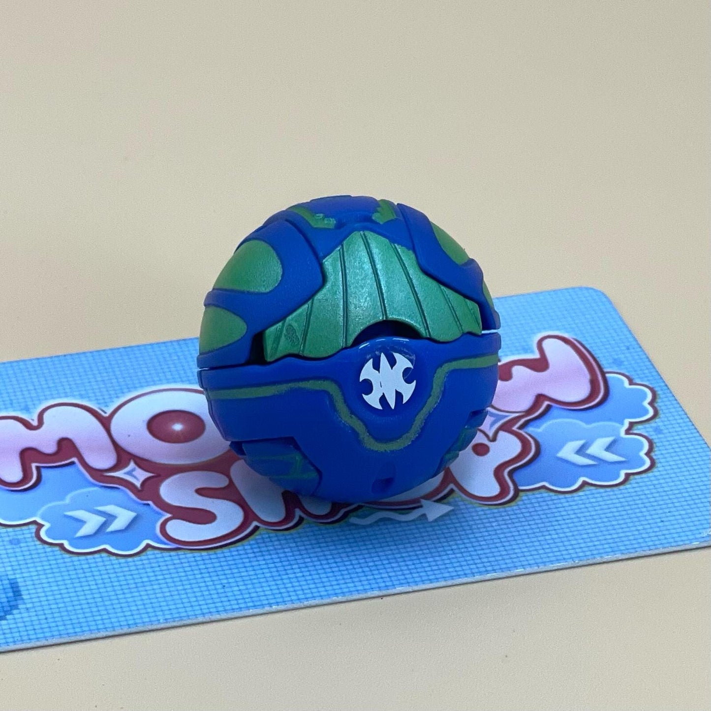 A blue and green toy, resembling a ball or a toy car, is sitting on a blue and white patterned surface.