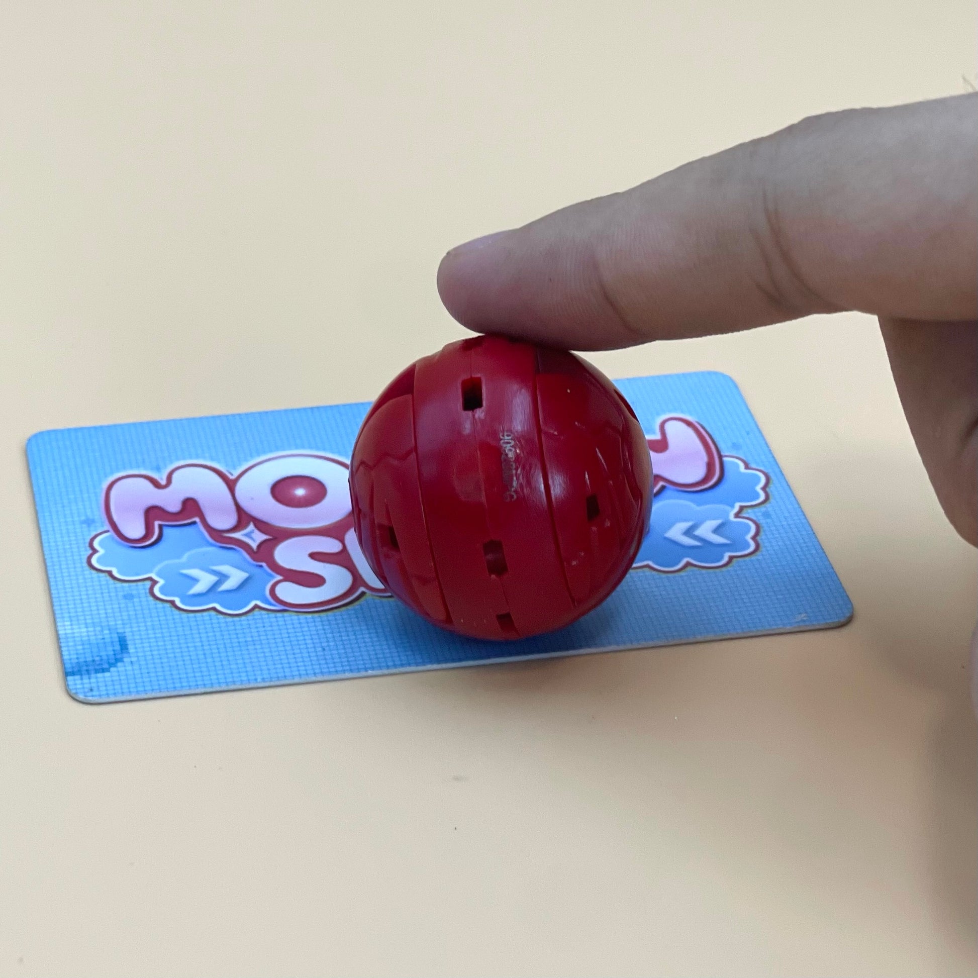 A hand is holding a red ball with a blue and white design on a light-colored surface.