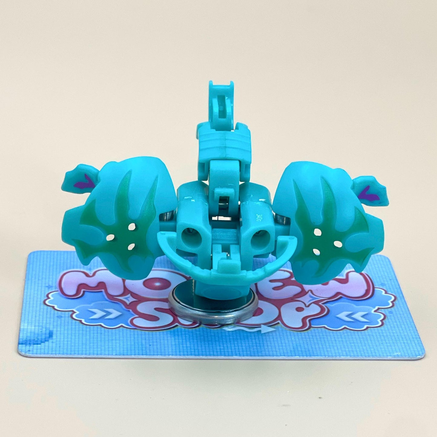 A toy in the shape of a blue and green monster with two arms and a head, sitting on a blue and white checkered surface.