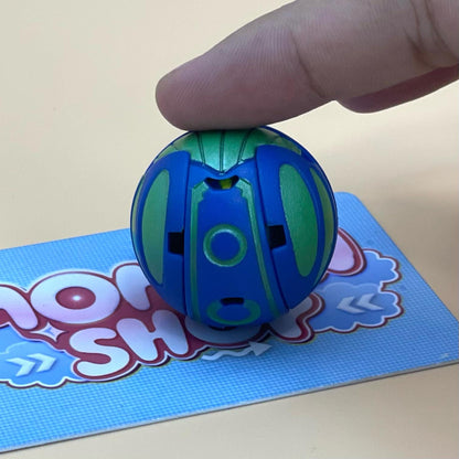 A hand is holding a blue and green toy, which appears to be a ball or a toy ball, on a blue surface with a partially visible text logo.