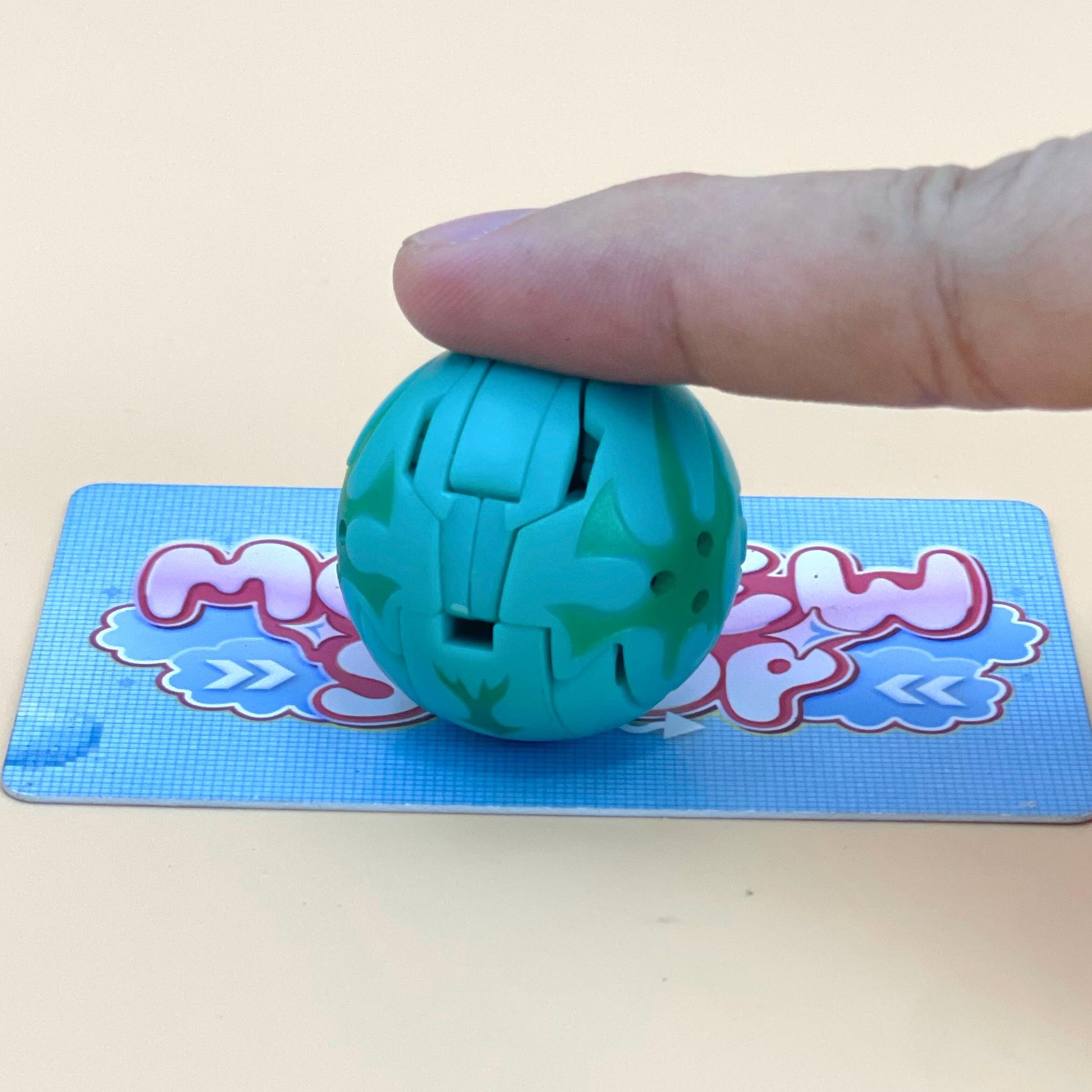 A hand is holding a green toy ball with a patterned design, placed on a blue and pink patterned surface.