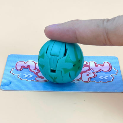A hand is holding a green toy ball with a patterned design, placed on a blue and pink patterned surface.