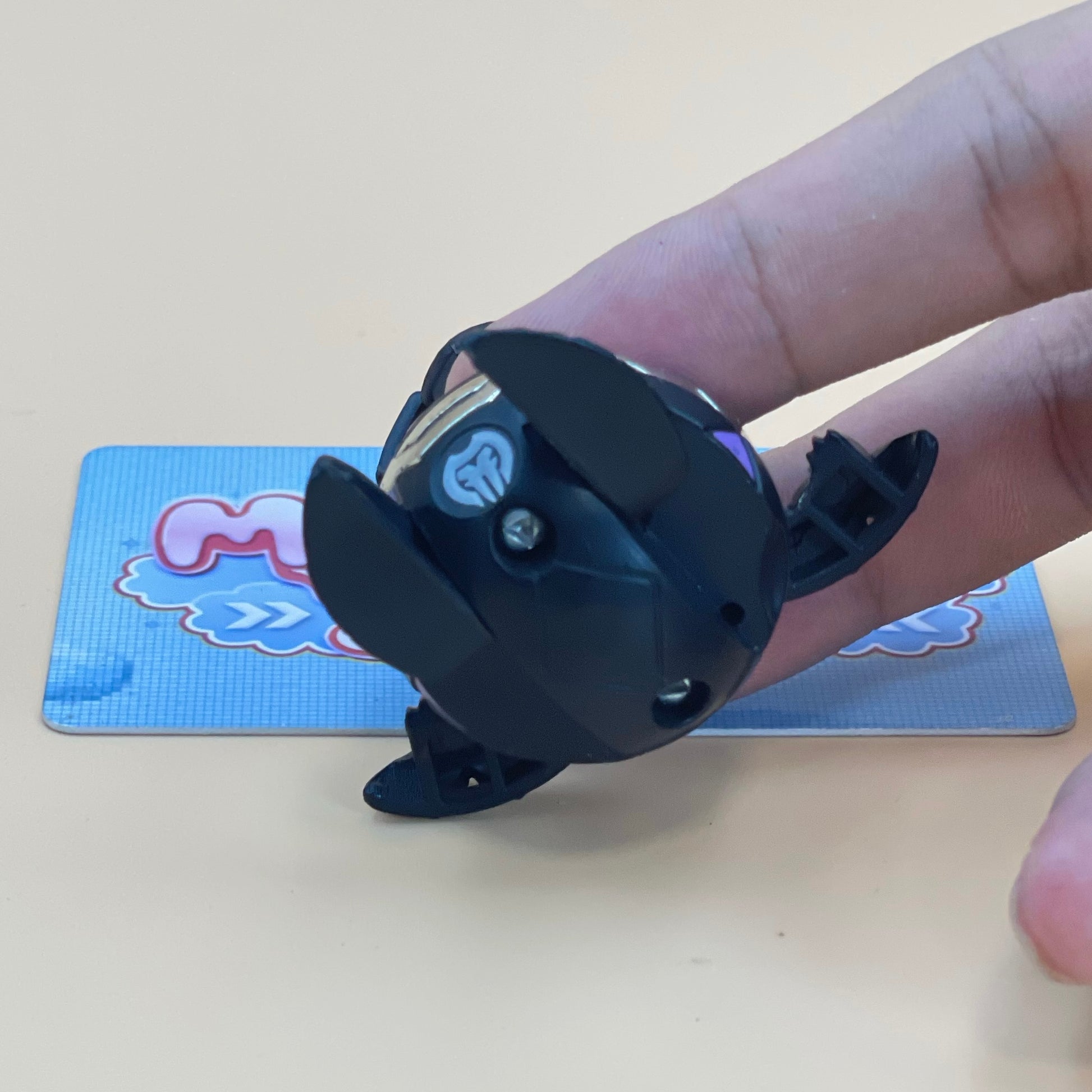 A person's hand is holding a black toy with a heart-shaped cutout on it, which appears to be a toy car or a small toy.