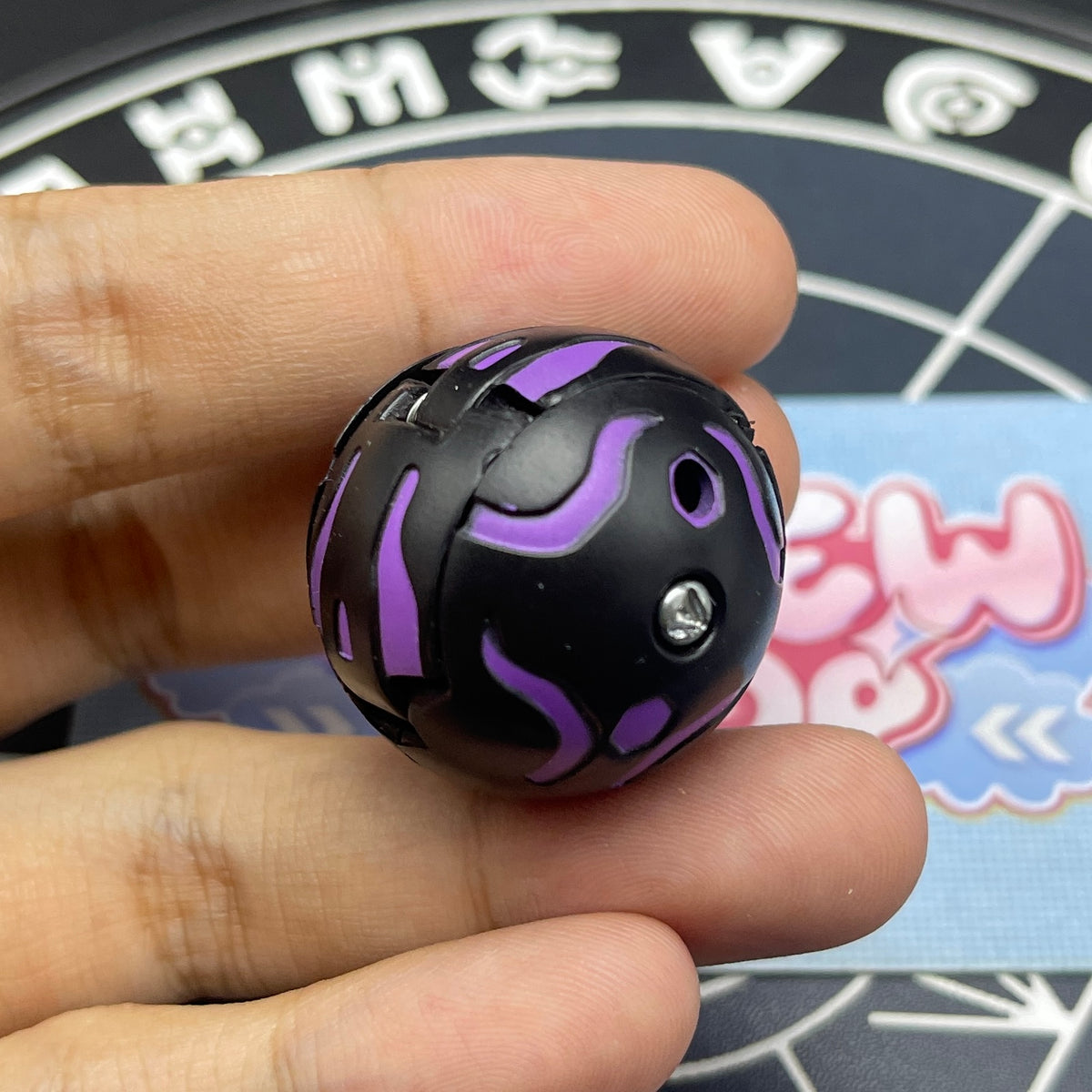 Closed sphere mode of Darkus B1 Centipoid Bakugan showing purple stripe patterns on black surface.
