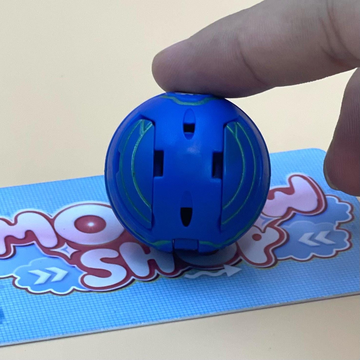 A person's hand is holding a blue plastic ball with a green design on it, which is placed on a blue and pink patterned surface.