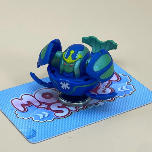 A toy figure of a blue and green robot-like character is sitting on a blue and white patterned surface.